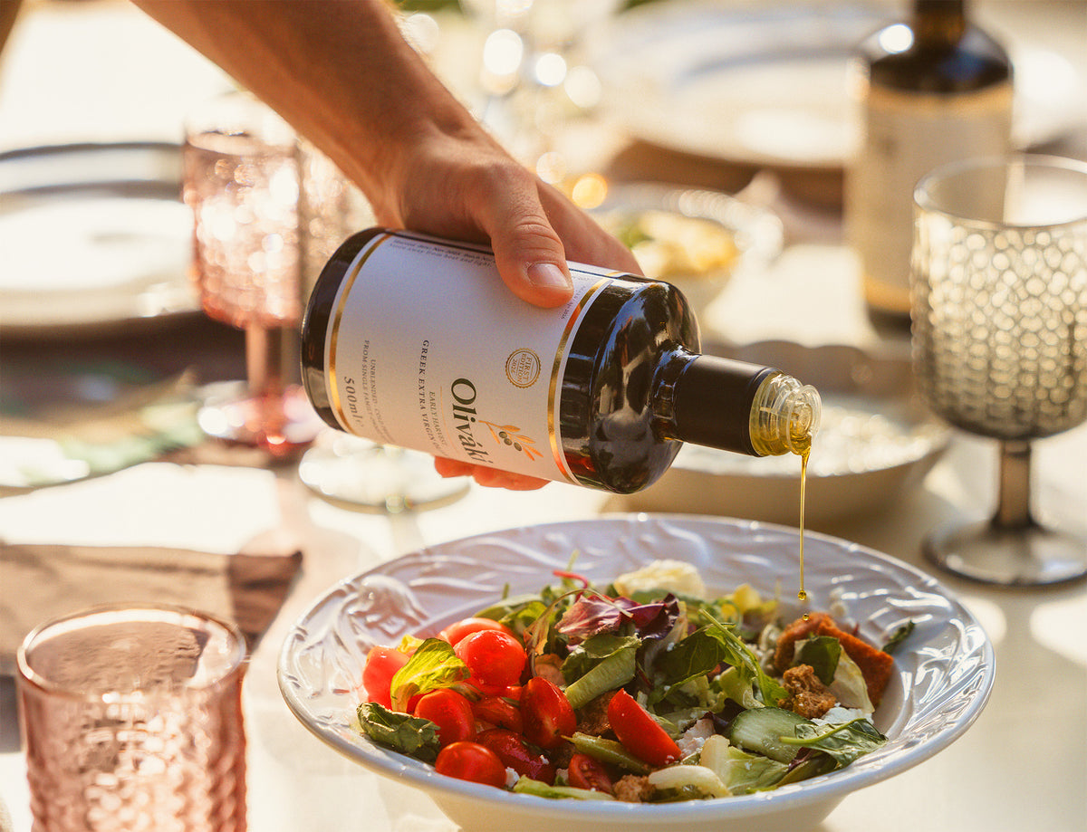 Hand pouring extra virgin olive oil from a dark bottle onto a fresh garden salad.