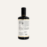 A dark glass bottle of olive oil with a black cap, showing the back of the label with nutrition facts and ingredients, on a white background.