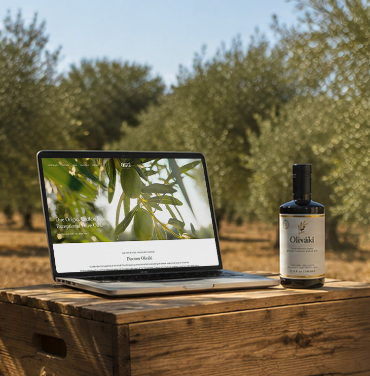 Laptop showing Small Olive website next to a bottle of Olivaki olive oil on a wooden crate.