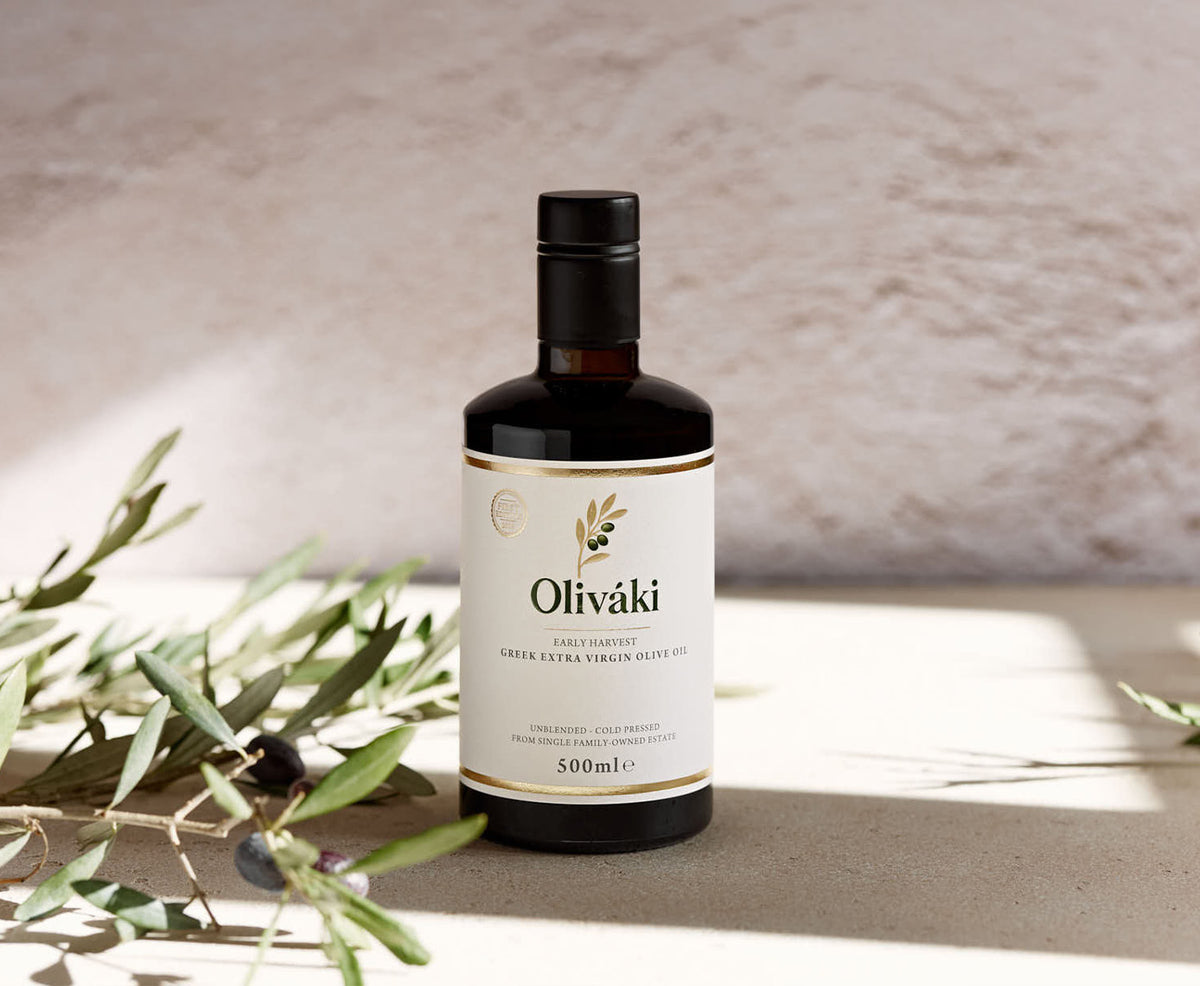 Bottle of Oliváki Early Harvest Greek Extra Virgin Olive Oil on a stone surface with olive leaves.