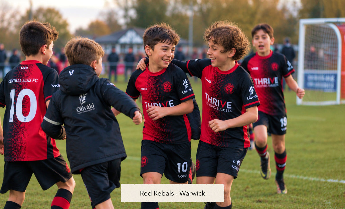 Young boys in red and black soccer uniforms celebrating a goal on a grass field.