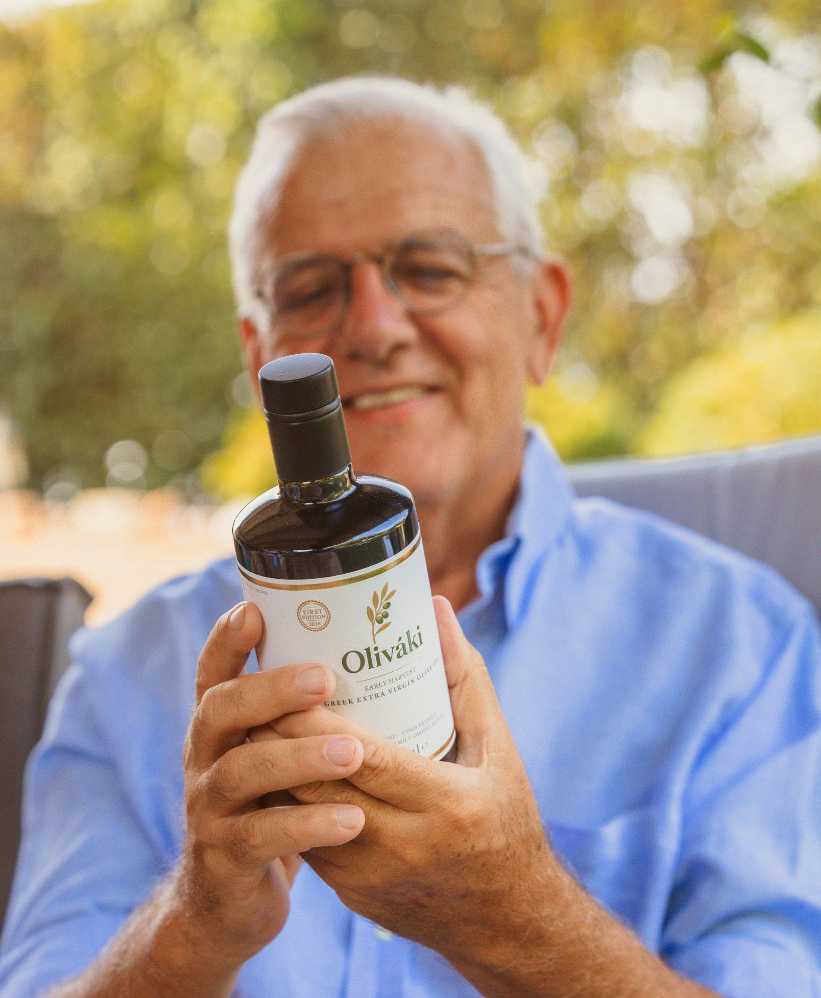 Smiling man holding a bottle of Oliváki Greek extra virgin olive oil outdoors.
