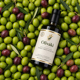 Oliváki Early Harvest Greek Extra Virgin Olive Oil bottle surrounded by fresh green and purple olives