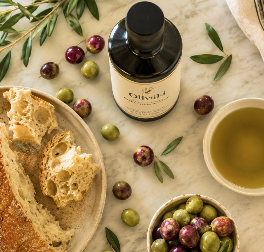 Oliváki Greek extra virgin olive oil bottle with olives and crusty bread on marble.