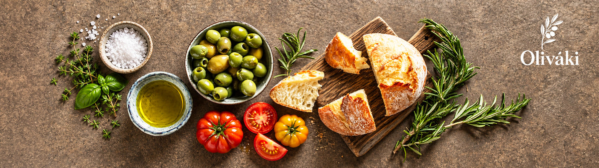 Fresh olives, crusty bread, olive oil, tomatoes, and herbs on a rustic stone surface.