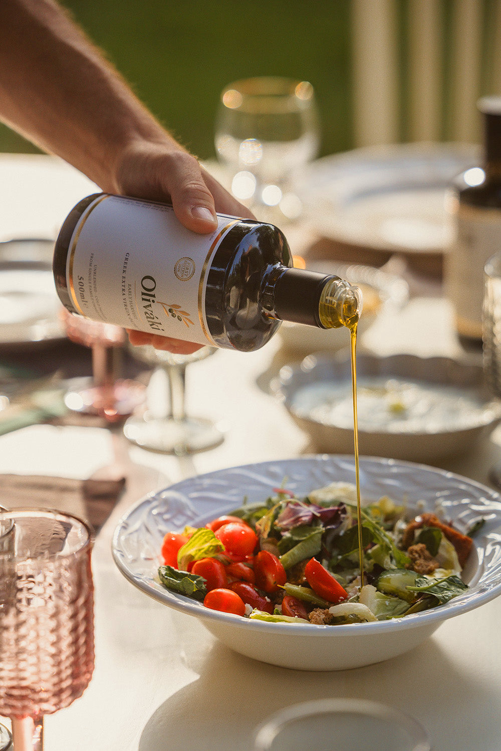 Pouring extra virgin olive oil from a dark bottle onto a fresh garden salad in a white bowl.