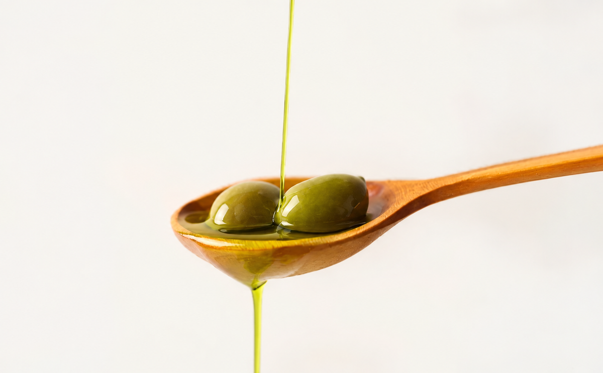 Green olives in a wooden spoon with extra virgin olive oil dripping.